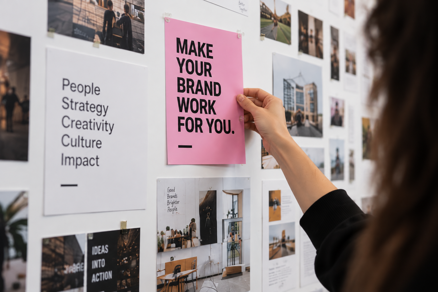 A hand pinning a pink poster reading Make Your Brand Work For You onto a wall of references